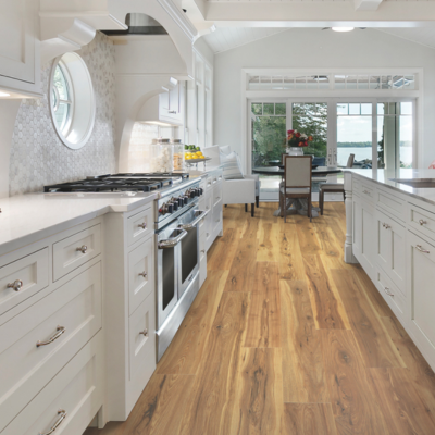 A bright kitchen and dining area with light brown laminate flooring, white cabinetry, a stainless steel range, and large windows overlooking water.